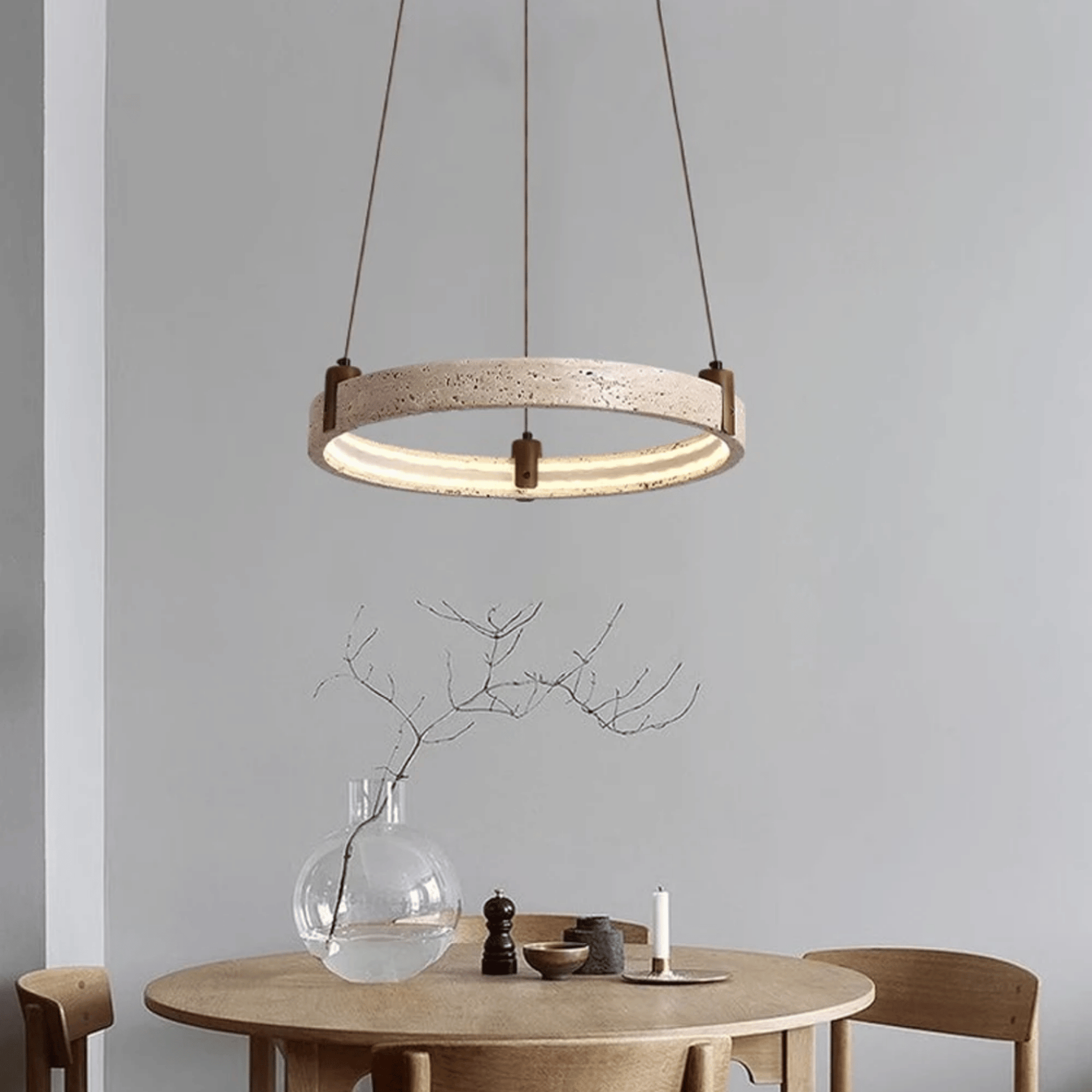 Modern pendant light hanging above a dining table with a vase and candle on a neutral background
