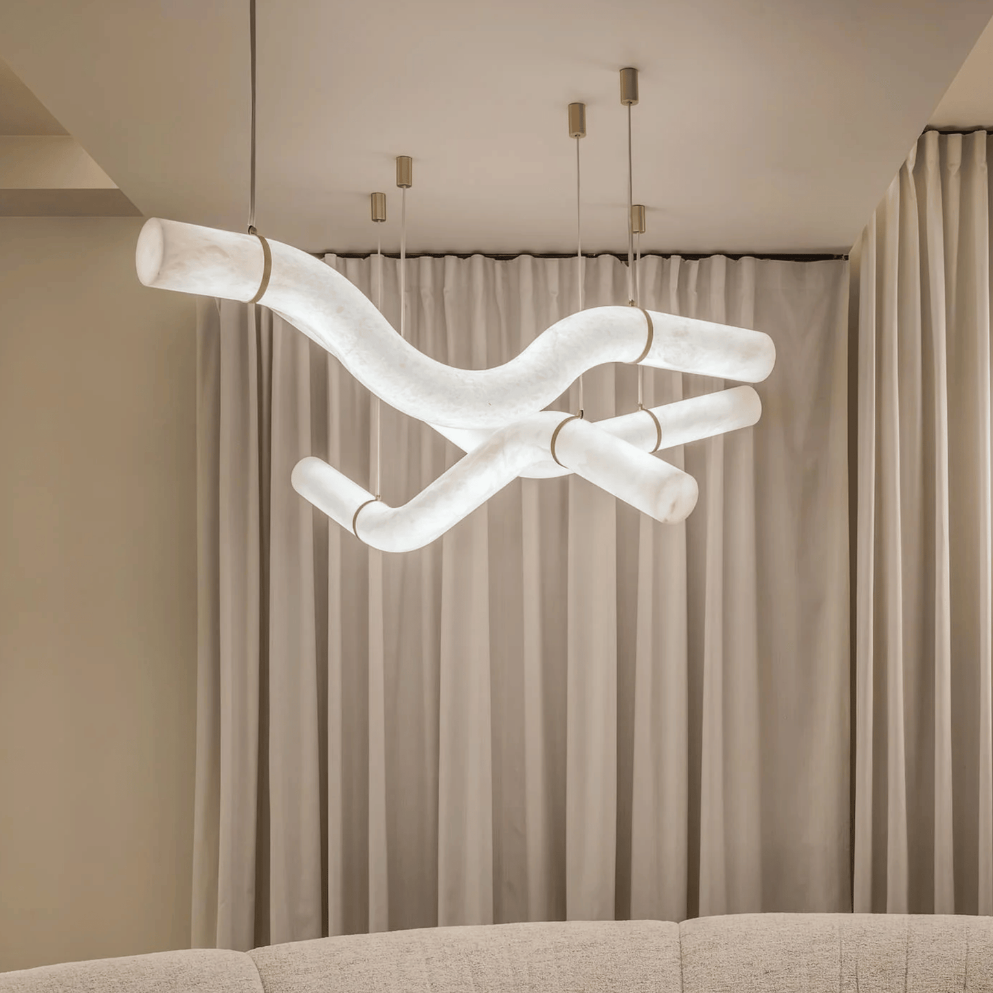 Modern chandelier hanging above a sofa with beige curtains in the background