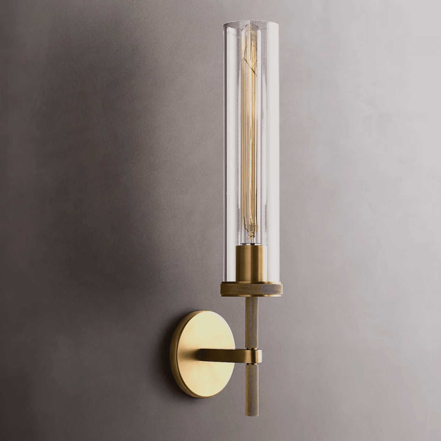 Wall-mounted light fixture with brass finish and clear glass on a gray wall.
