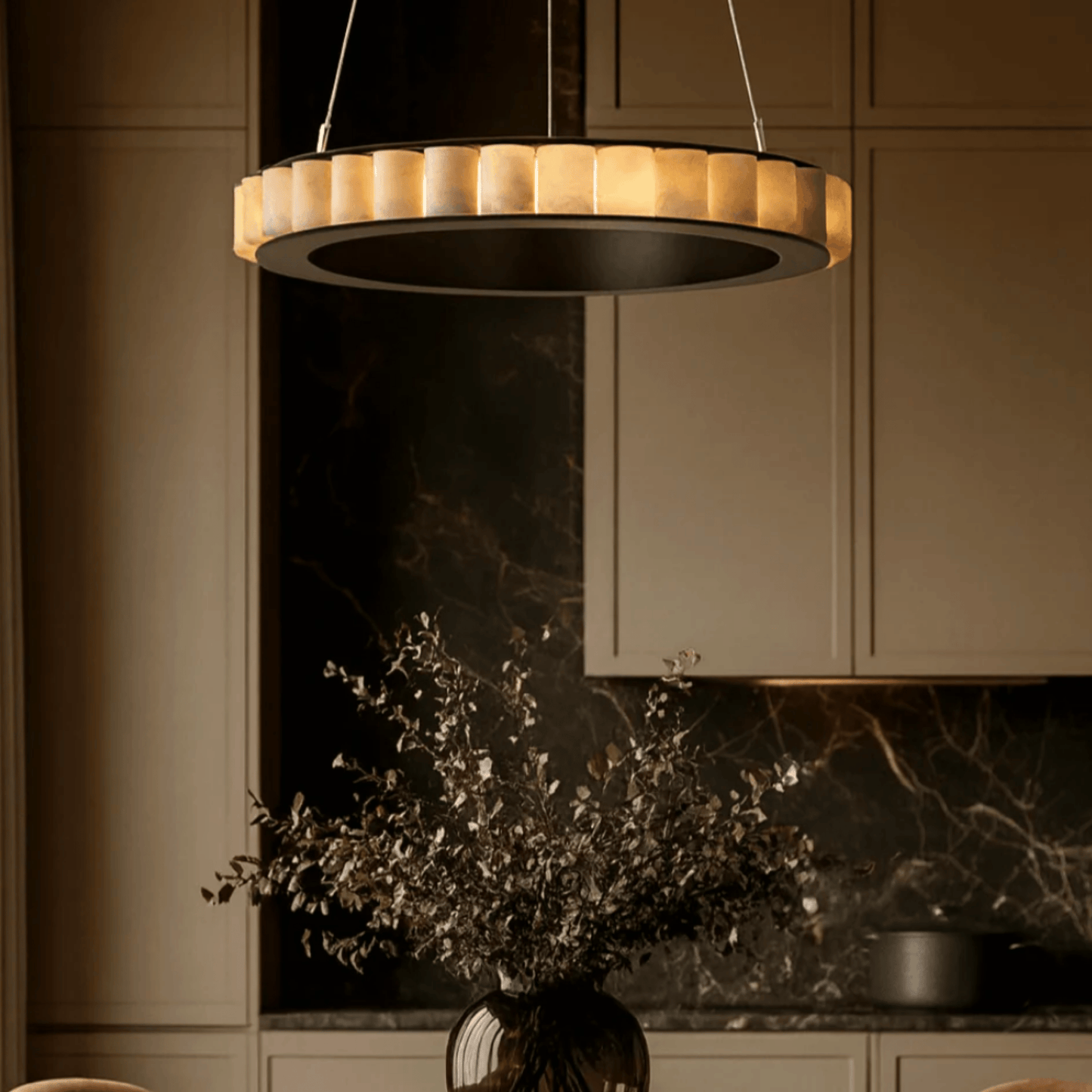 Modern pendant light hanging in a kitchen with marble backsplash and neutral cabinets.
