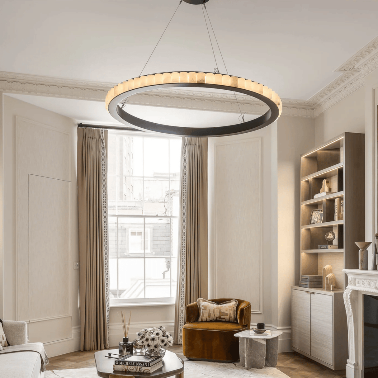 Modern living room with a large circular chandelier, bookshelf, and armchair.