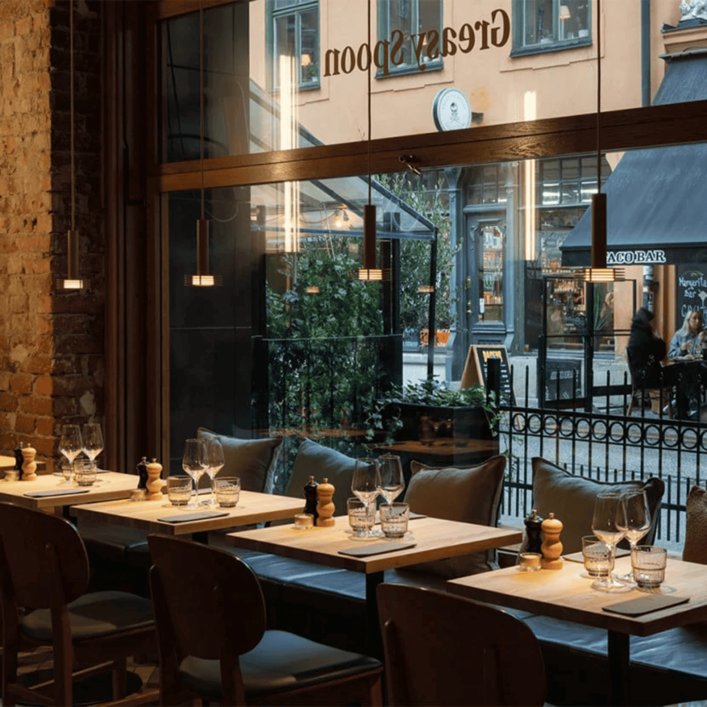 Restaurant interior with tables, chairs, and wine glasses outside a glass door.