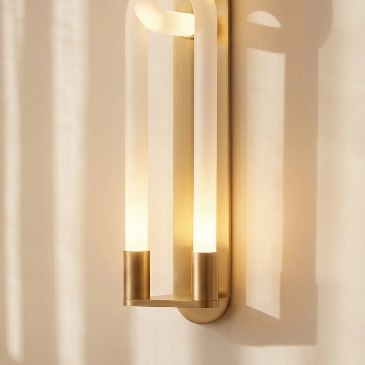 Modern wall sconce with gold finish and glass shade on a neutral wall.