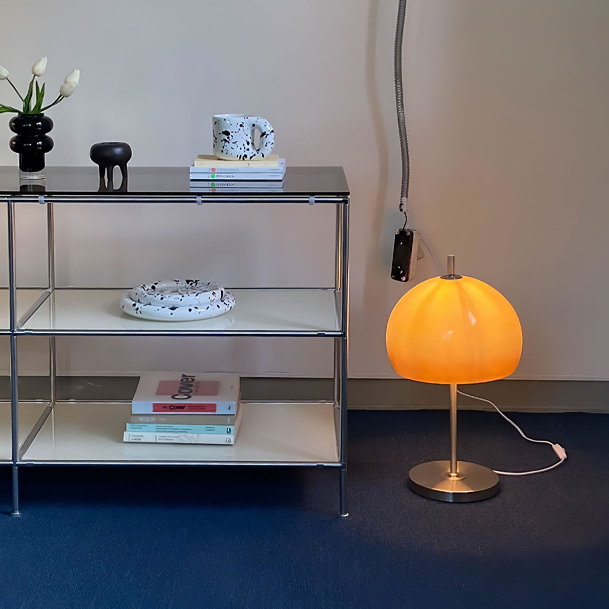 A stylish orange globe-shaped lamp placed on a desk, with a view of city buildings visible through the window in the background.