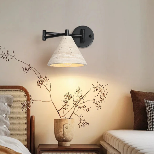 The same wall lamp installed above a bed, glowing softly over floral wall art and neutral bedding.