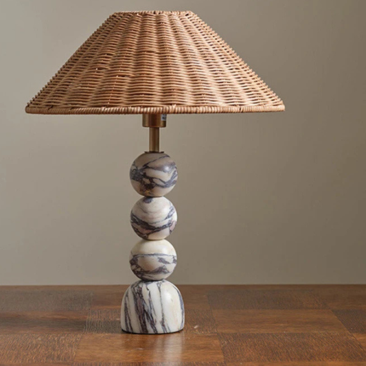 The same lamp on a wooden table in natural lighting, highlighting the marble base and wicker texture.
