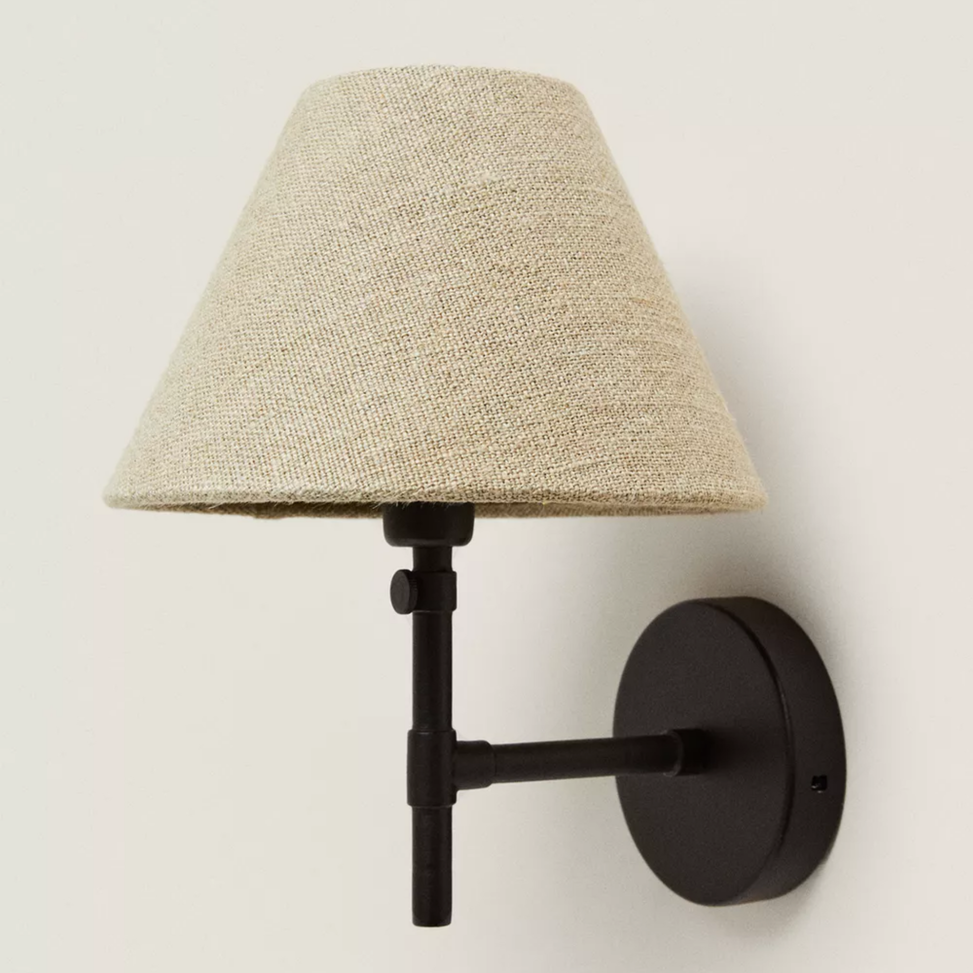 Wall-mounted lamp with a beige shade and black metal fixture on a light gray background