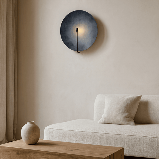Modern wall sconce above a beige sofa with a wooden coffee table and ceramic vase.