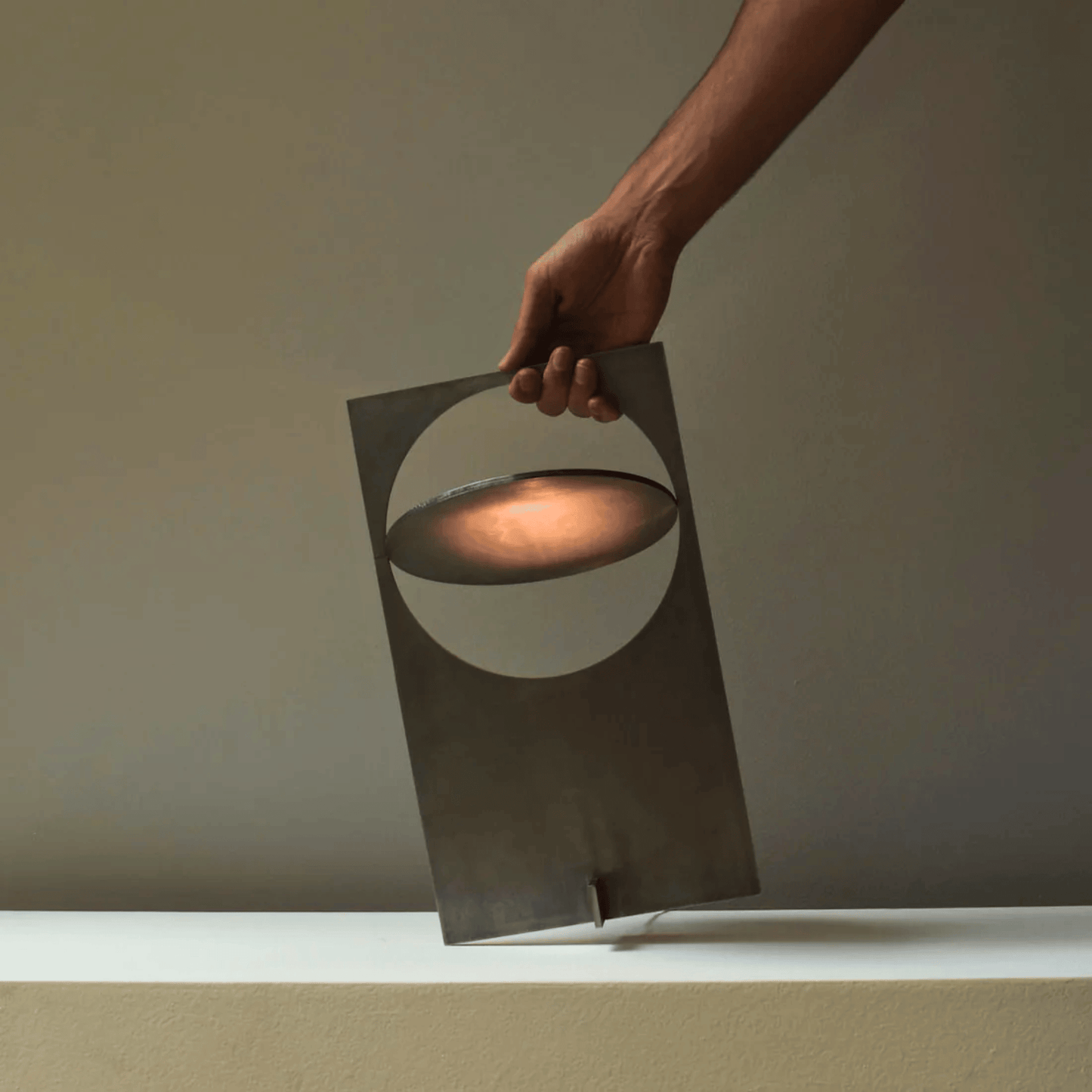 Hand holding a modern metal lantern with a warm glow against a neutral background