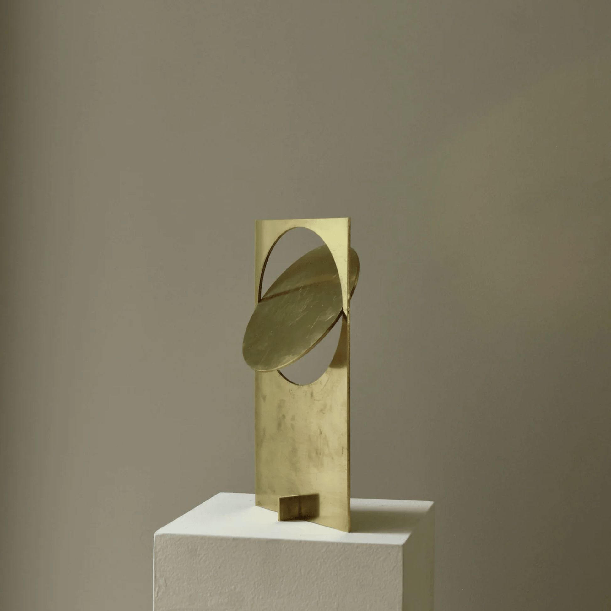 Gold abstract sculpture on a white pedestal against a beige background