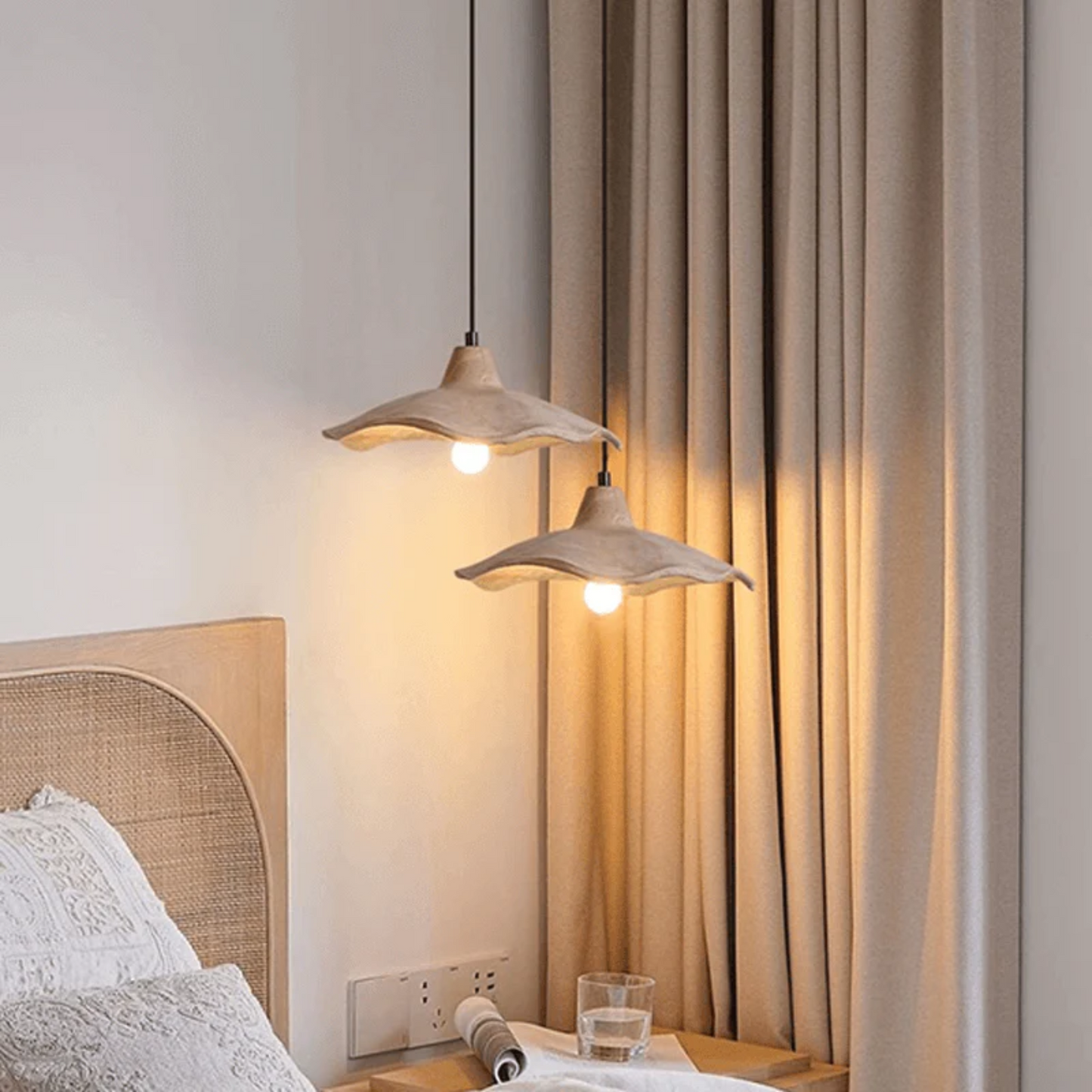 Two pendant lights hanging above a bed with beige curtains in the background.