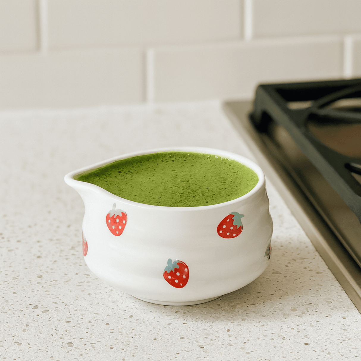 White ceramic pitcher with strawberry design filled with green liquid on a kitchen counter.