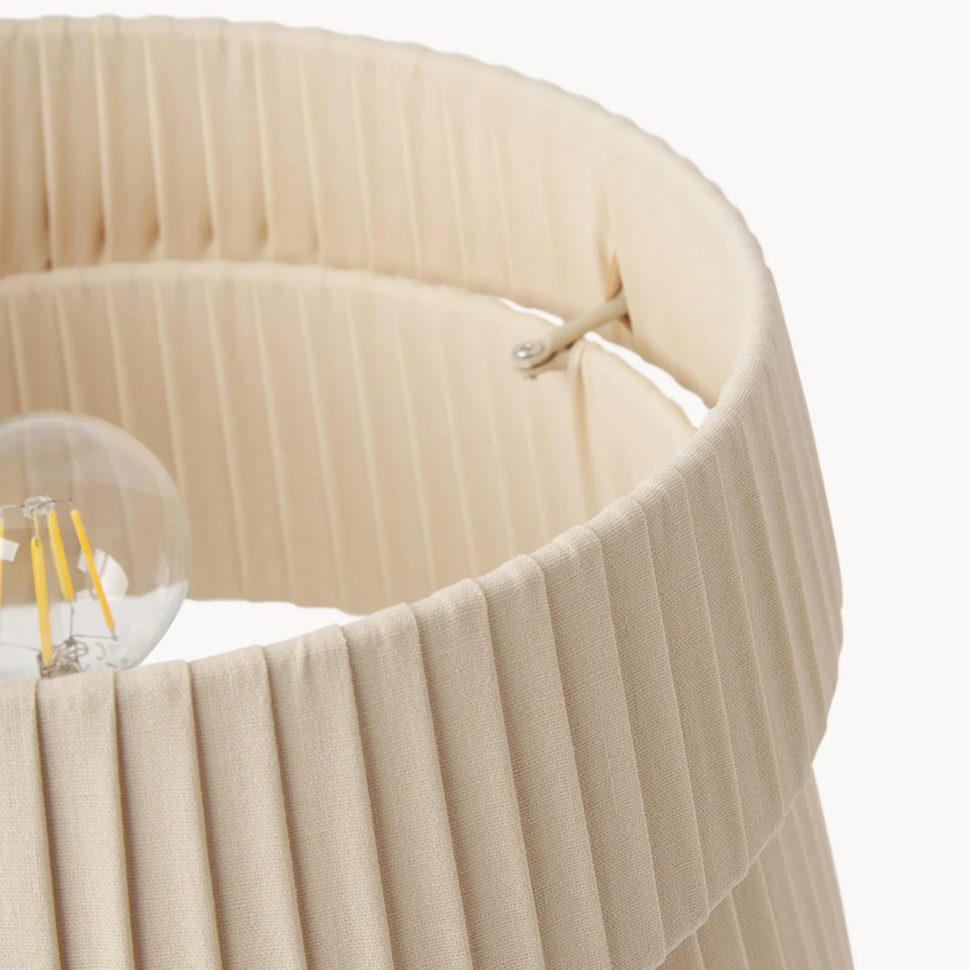 Close-up of a beige pleated lampshade with a light bulb inside on a white background