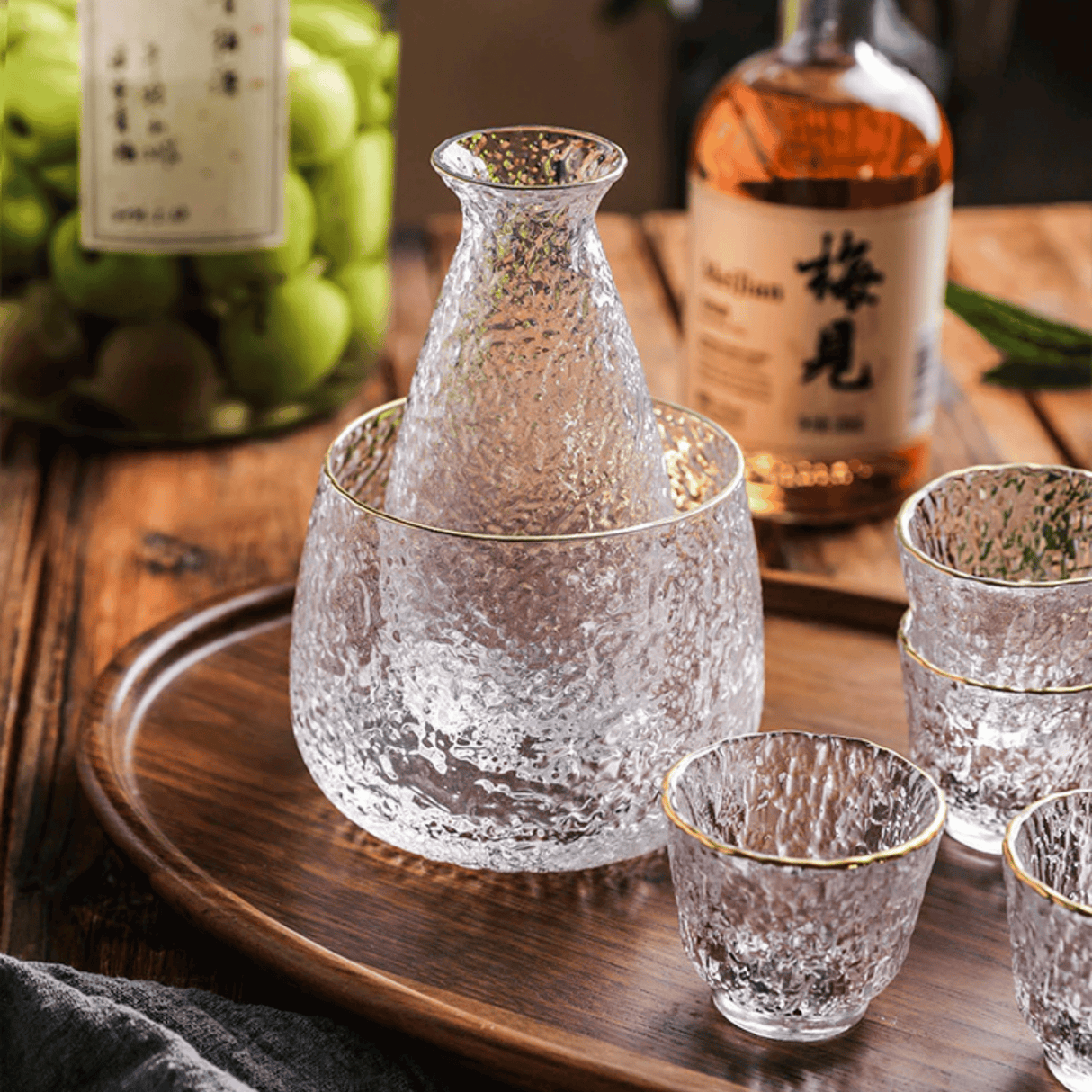 Clear glass sake set with a wooden tray and bottles in the background