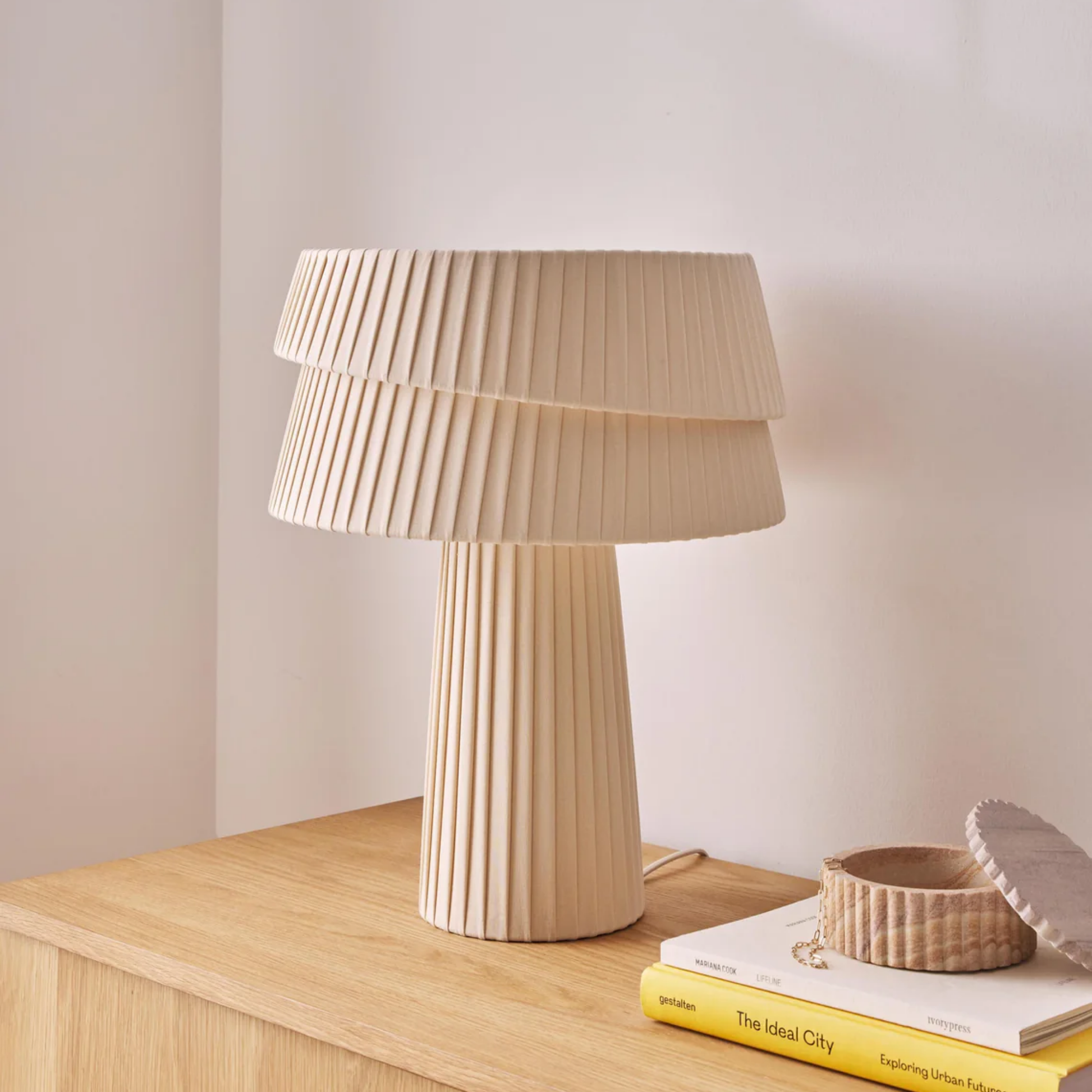 Beige table lamp on a wooden surface with books and a small bowl.