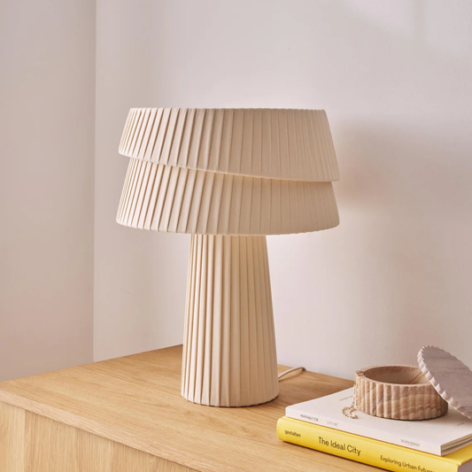 Beige table lamp on a wooden surface with books and a small bowl.