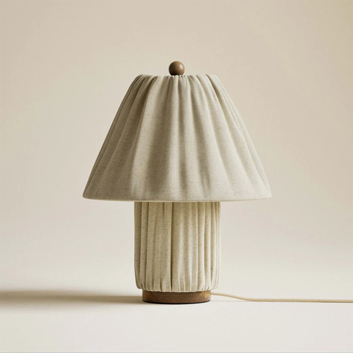 Table lamp with a pleated beige base and shade on a plain background