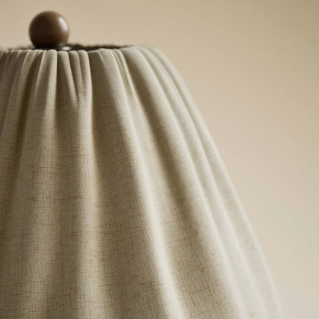 Close-up of a textured beige lampshade with a wooden finial on a neutral background
