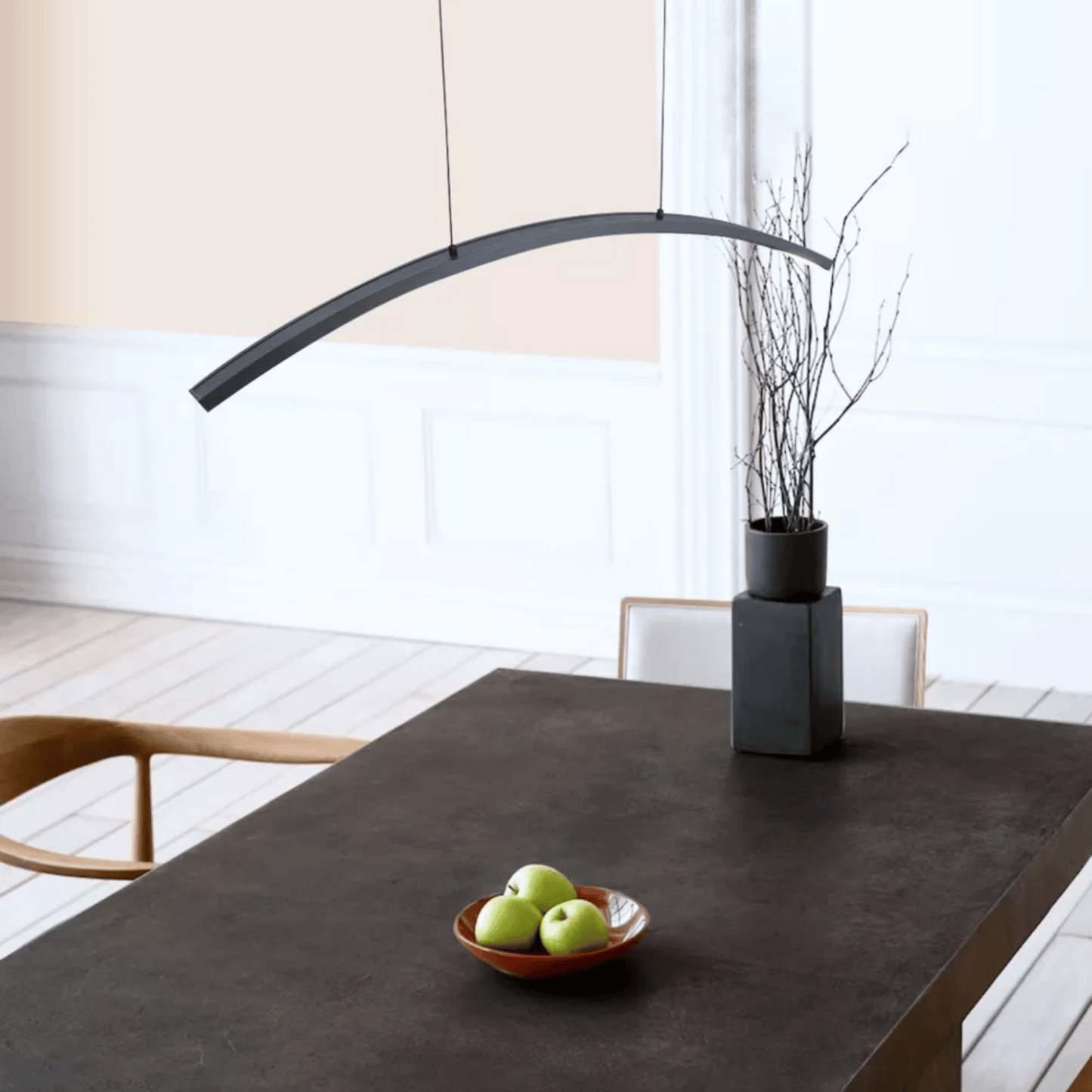 Modern dining table with a bowl of apples and a vase in a minimalistic room.