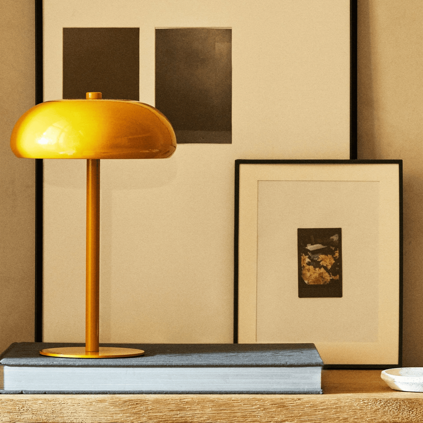 Yellow table lamp on a wooden surface with framed artwork in the background
