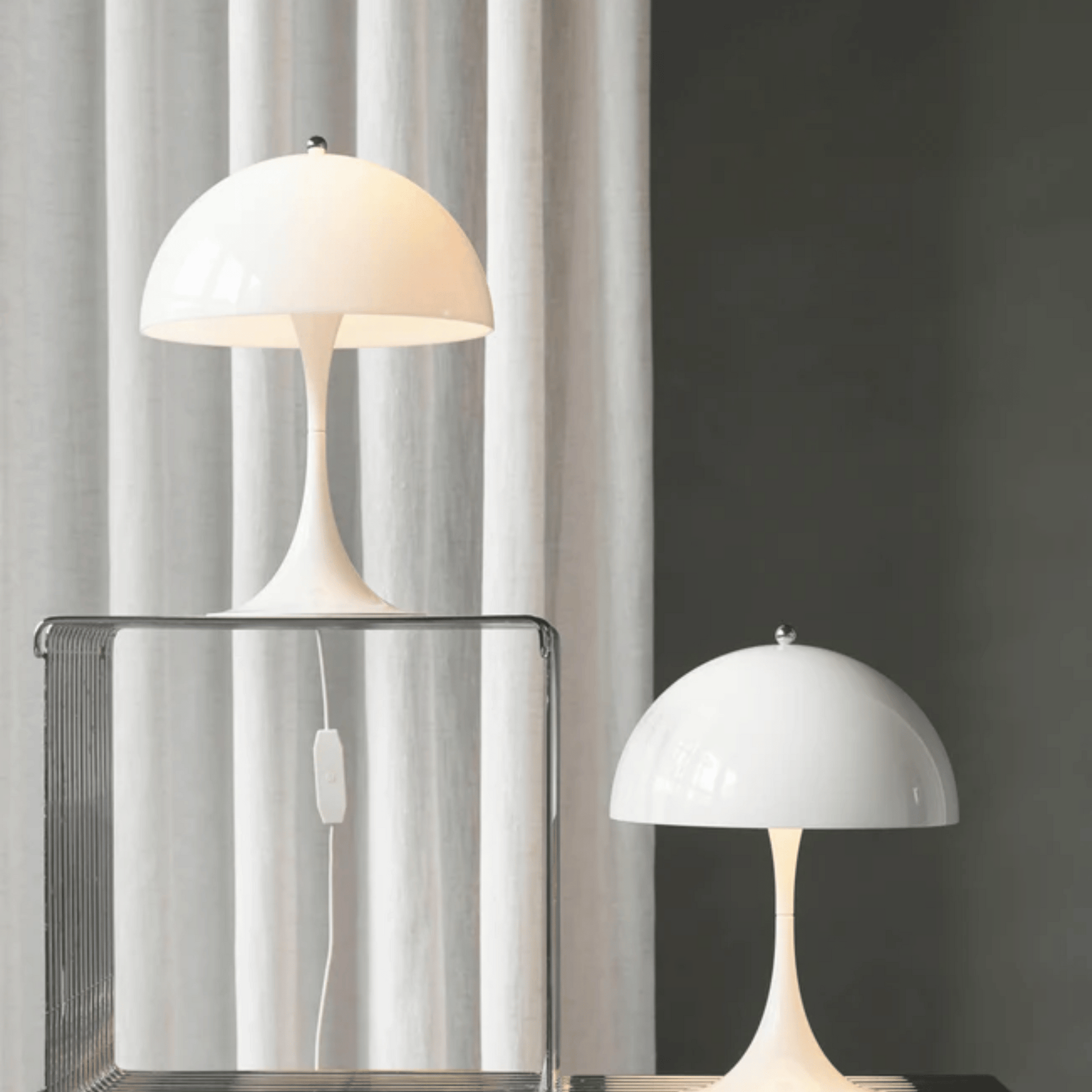 Two white table lamps on a dark surface with a light gray curtain in the background
