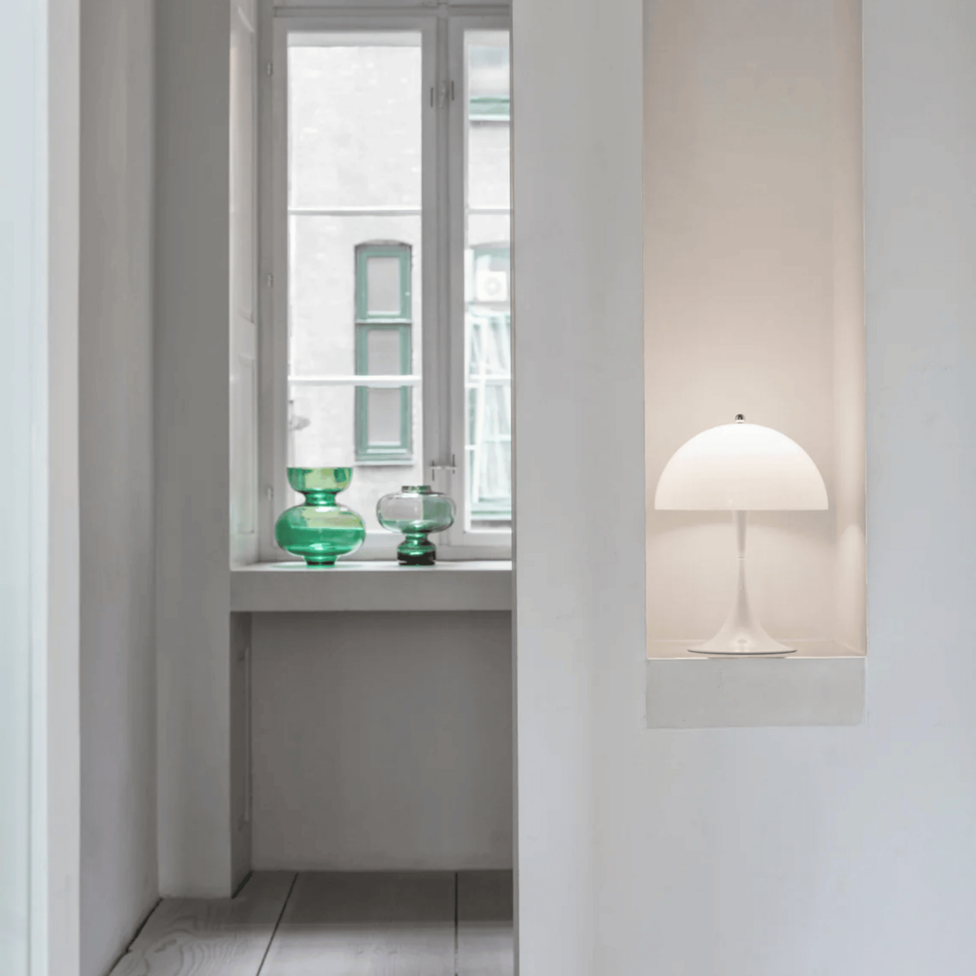 Modern interior with a white lamp and green glass vases on a windowsill.