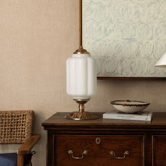 Decorative table lamp on a wooden side table with a textured wall and framed artwork in the background.