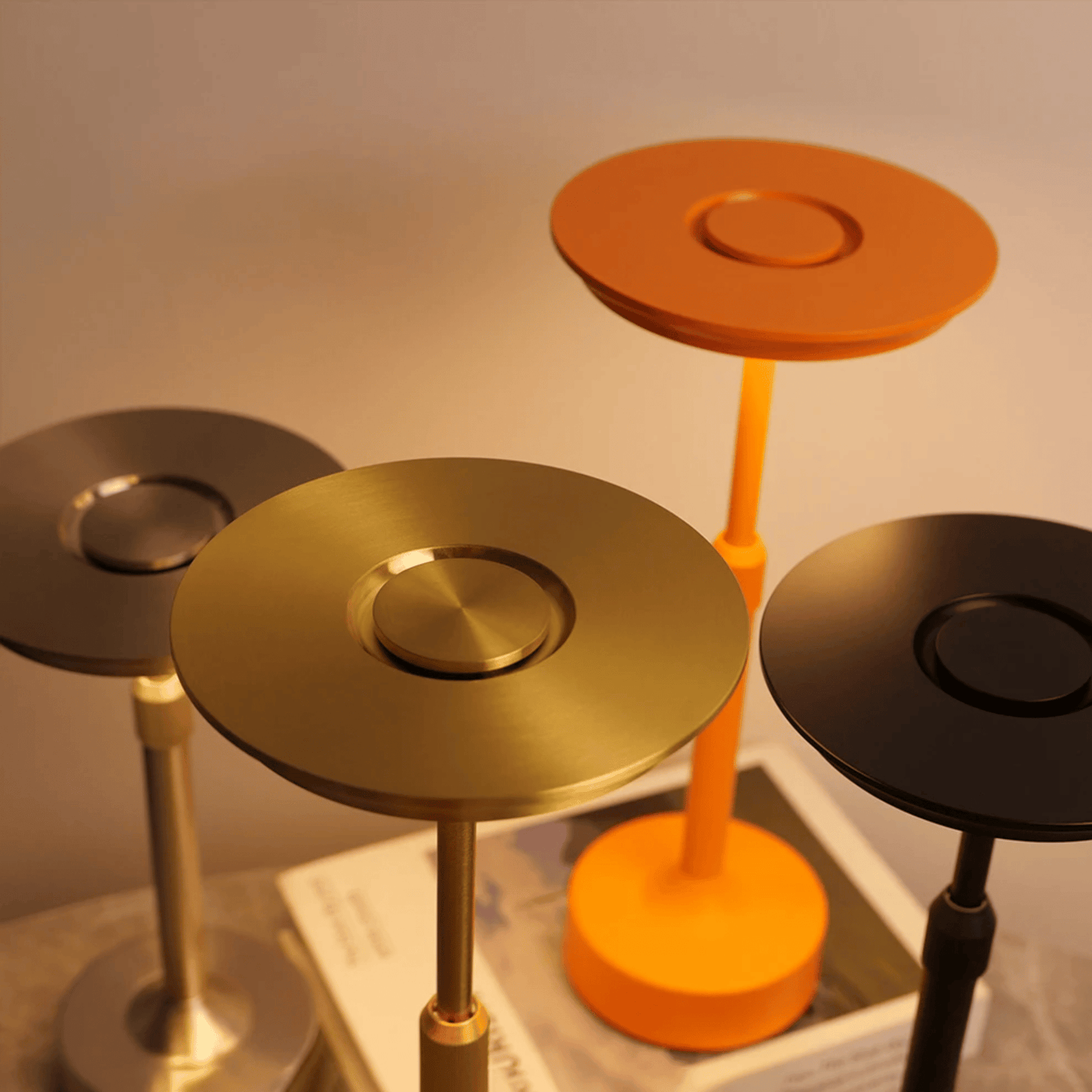 Set of four round stools in gold, orange, black, and silver on a white surface.