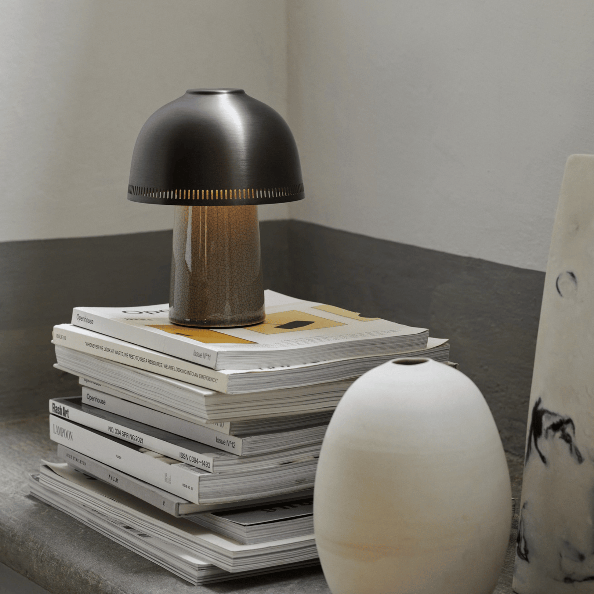 Small black lamp on a stack of books with a white vase in the foreground