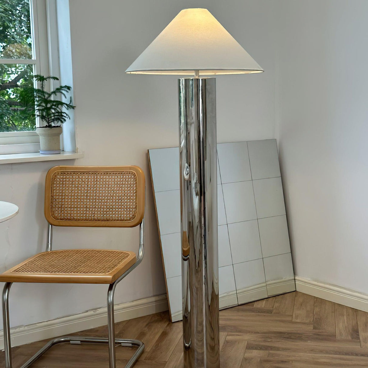 reflective chrome floor lamp beside a sofa with a white lampshade and indoor plants