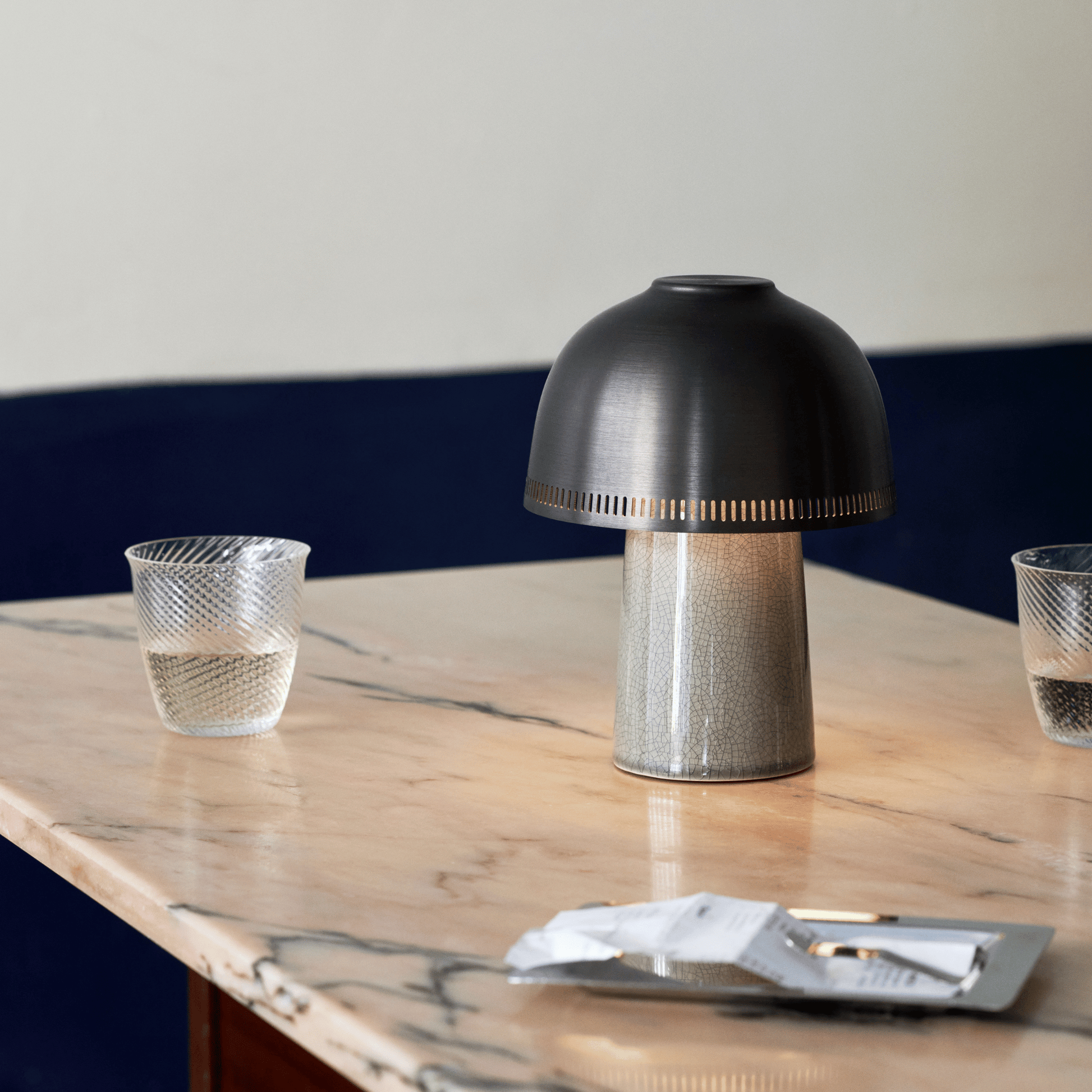 Black table lamp on a marble surface with two glasses and a small plate.