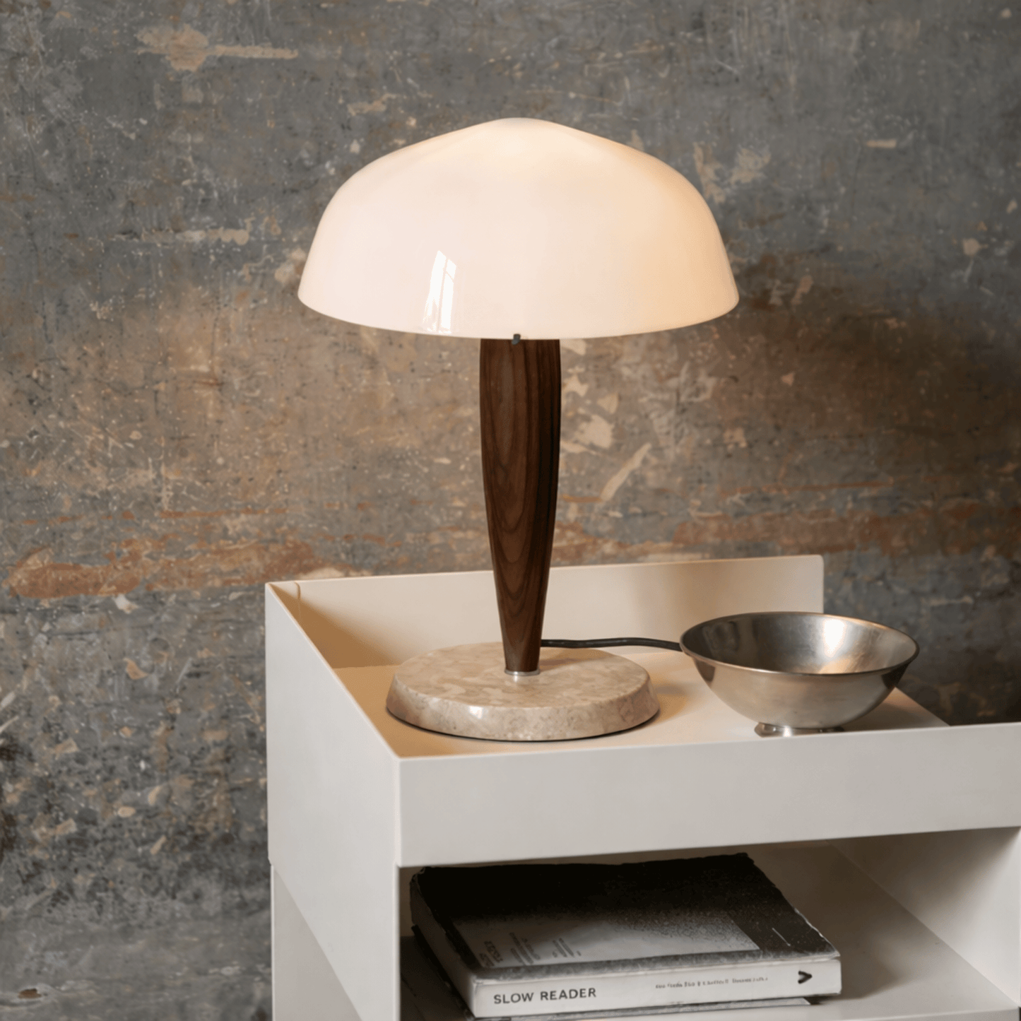 Table lamp with wooden base and white shade on a white surface against a textured wall.