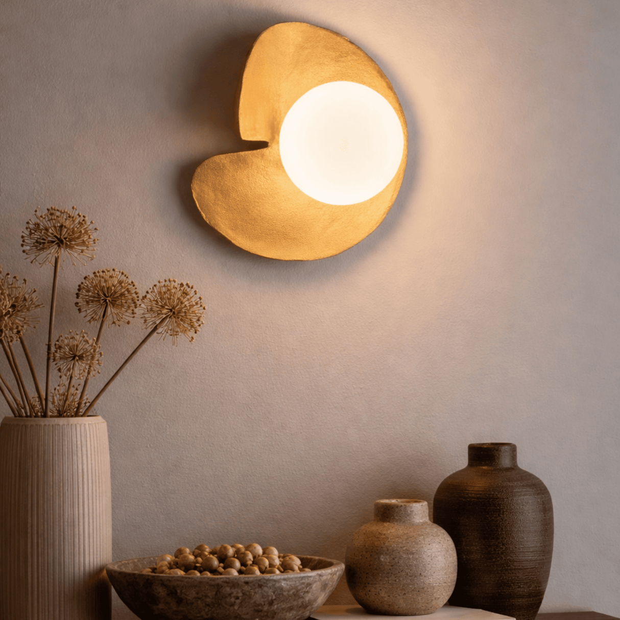 Decorative wall light fixture with a warm glow, surrounded by rustic vases and a bowl on a neutral background.