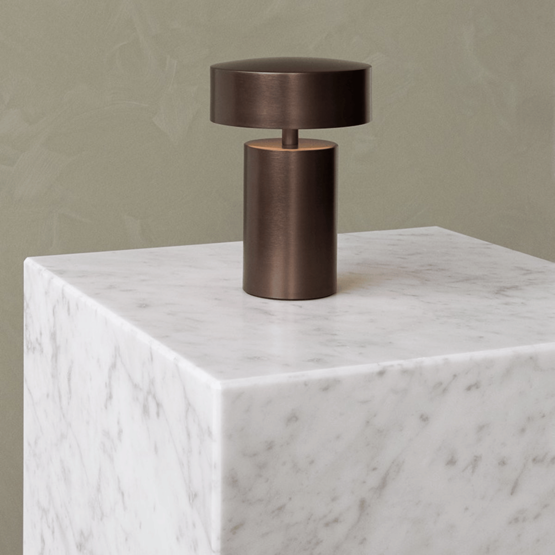 Bronze table lamp on a marble pedestal against a beige wall