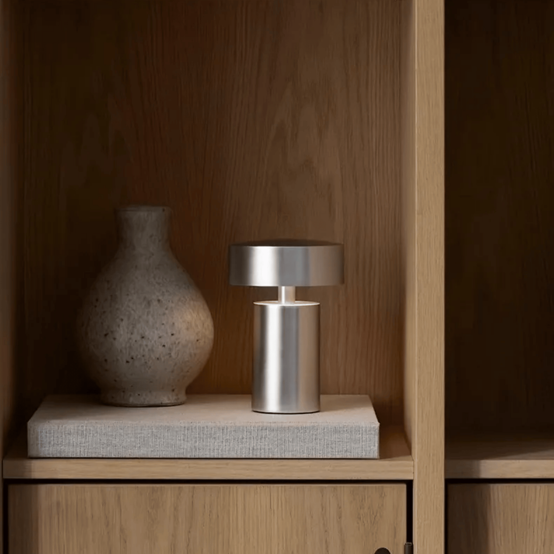 Silver lamp and textured vase on a wooden shelf