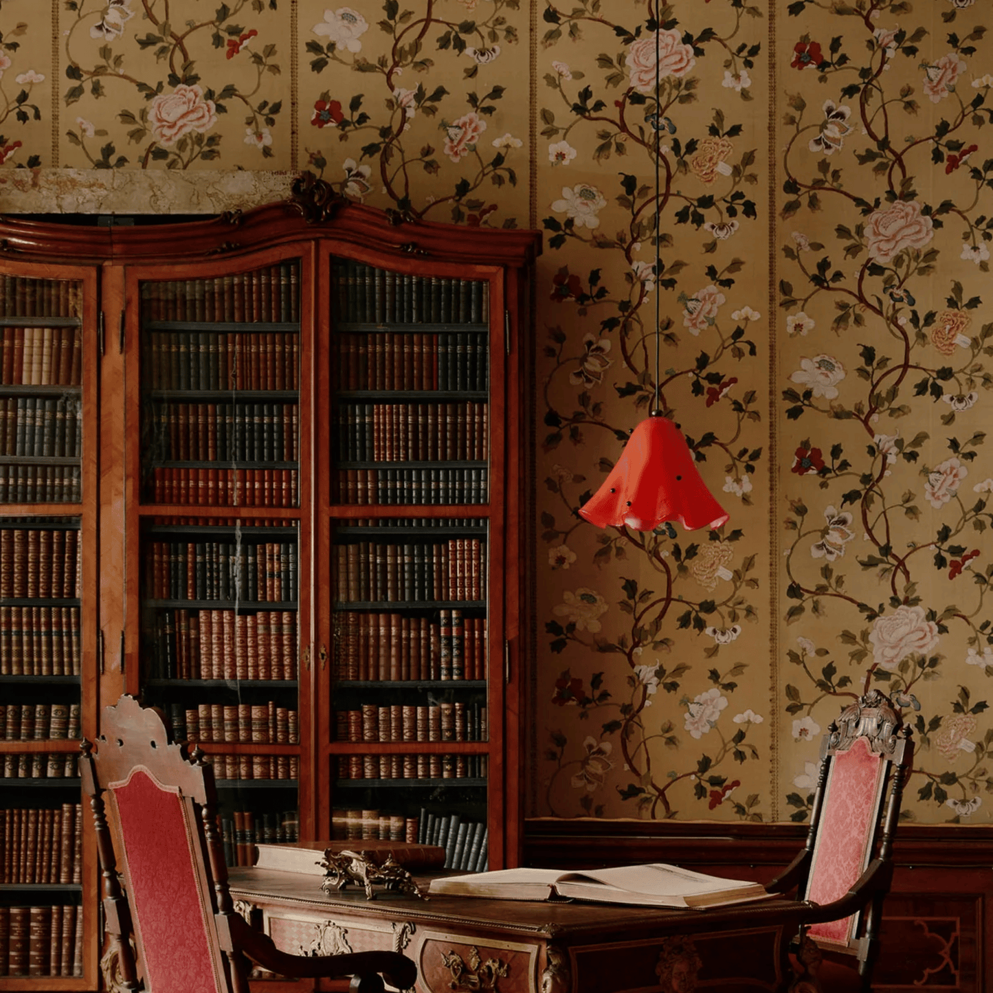 Vintage room with wooden bookshelf, floral wallpaper, and red lamp.
