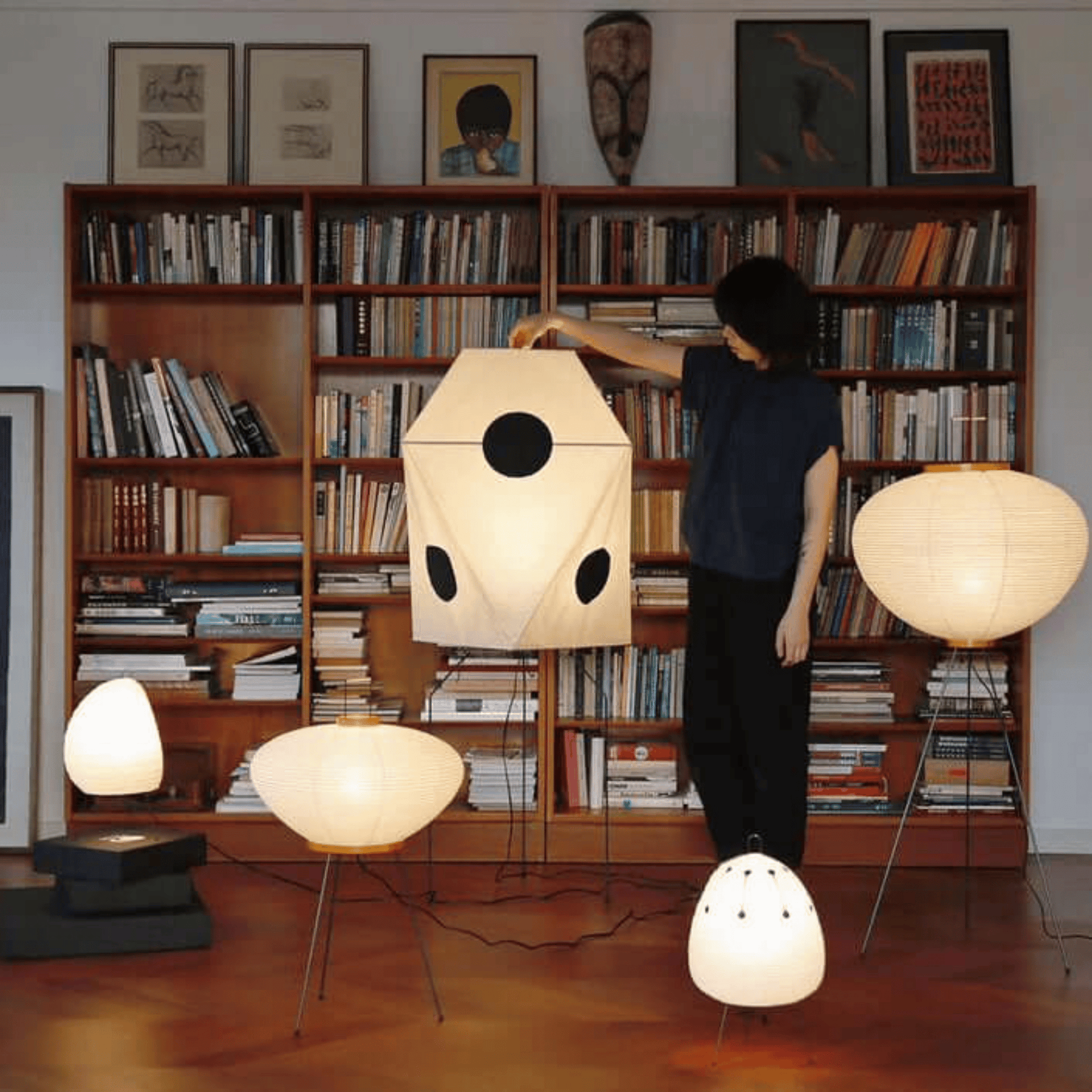 Person interacting with modern lamps in a room filled with bookshelves.