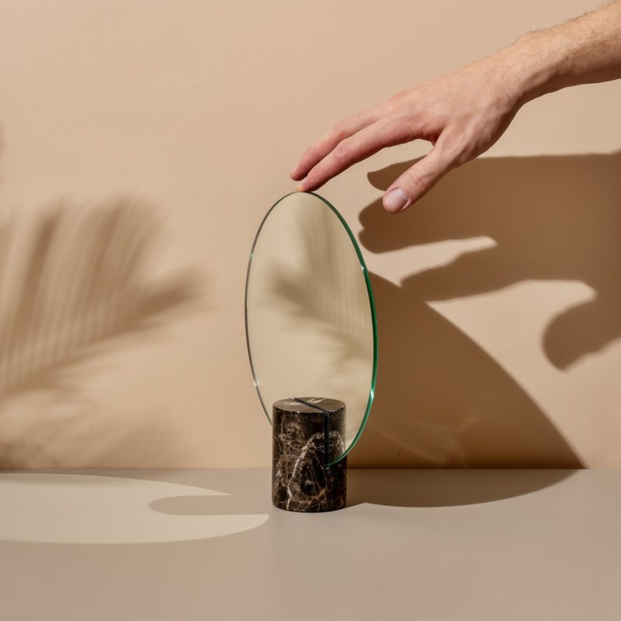 Hand reaching towards a round mirror on a beige surface with a neutral background