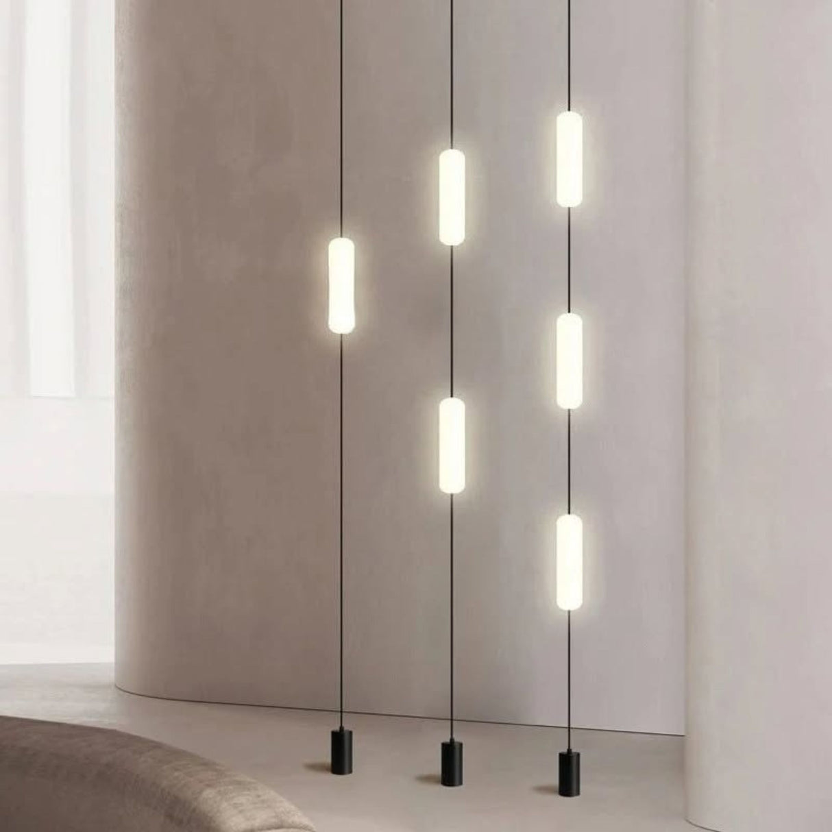 Multiple vertical tube pendant lights hanging in a row from the ceiling, casting warm light in a modern interior.
