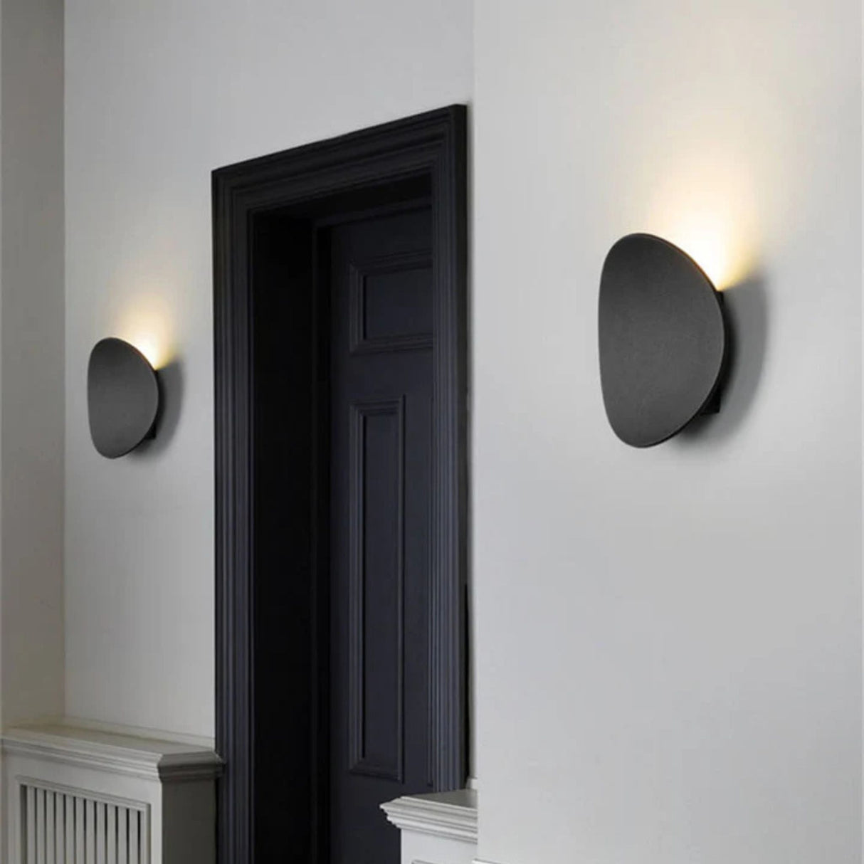 A black circular wall lamp glowing on a white wall near a dark doorway in a contemporary interior.
