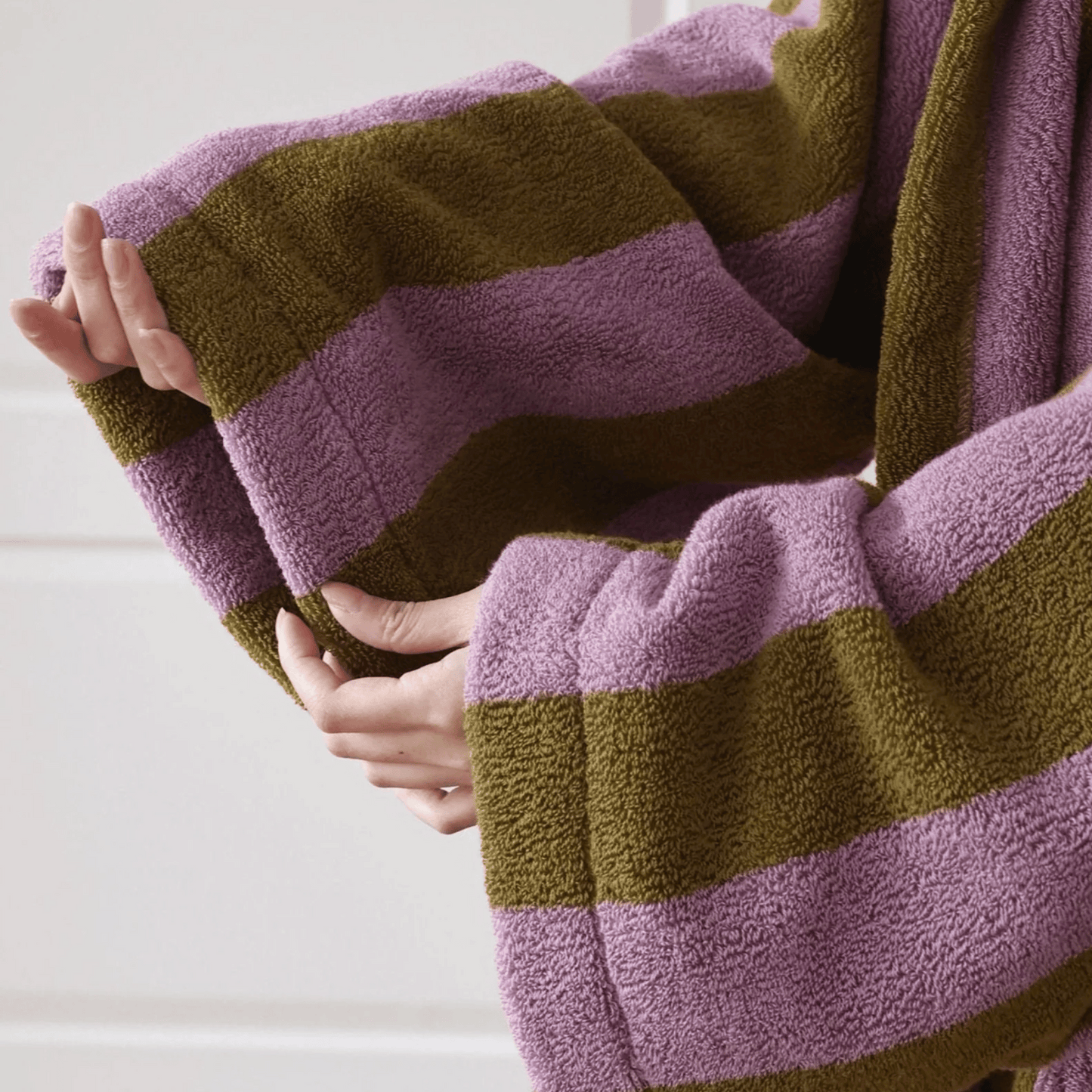 Close-up of hands holding a striped purple and green towel.