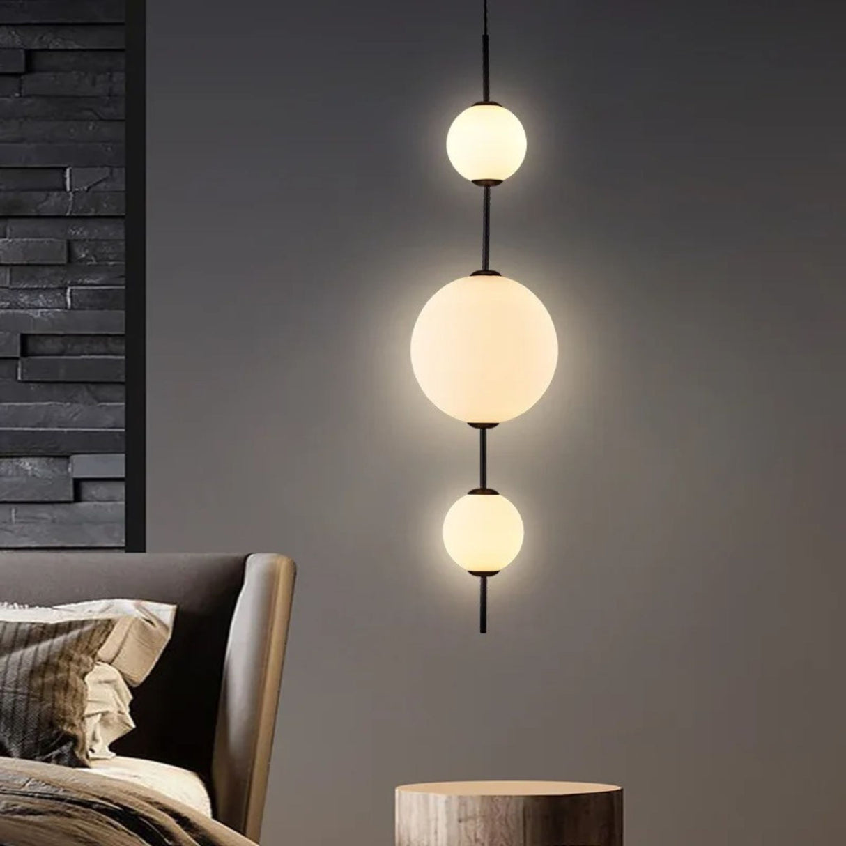 A modern bedroom with a set of three glowing globe pendant lights in the background above a bed with neutral tones.