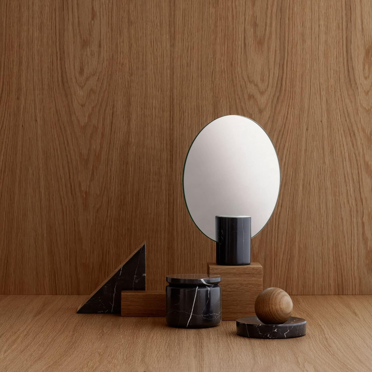 Small round mirror on a wooden stand with decorative items against a wooden wall.