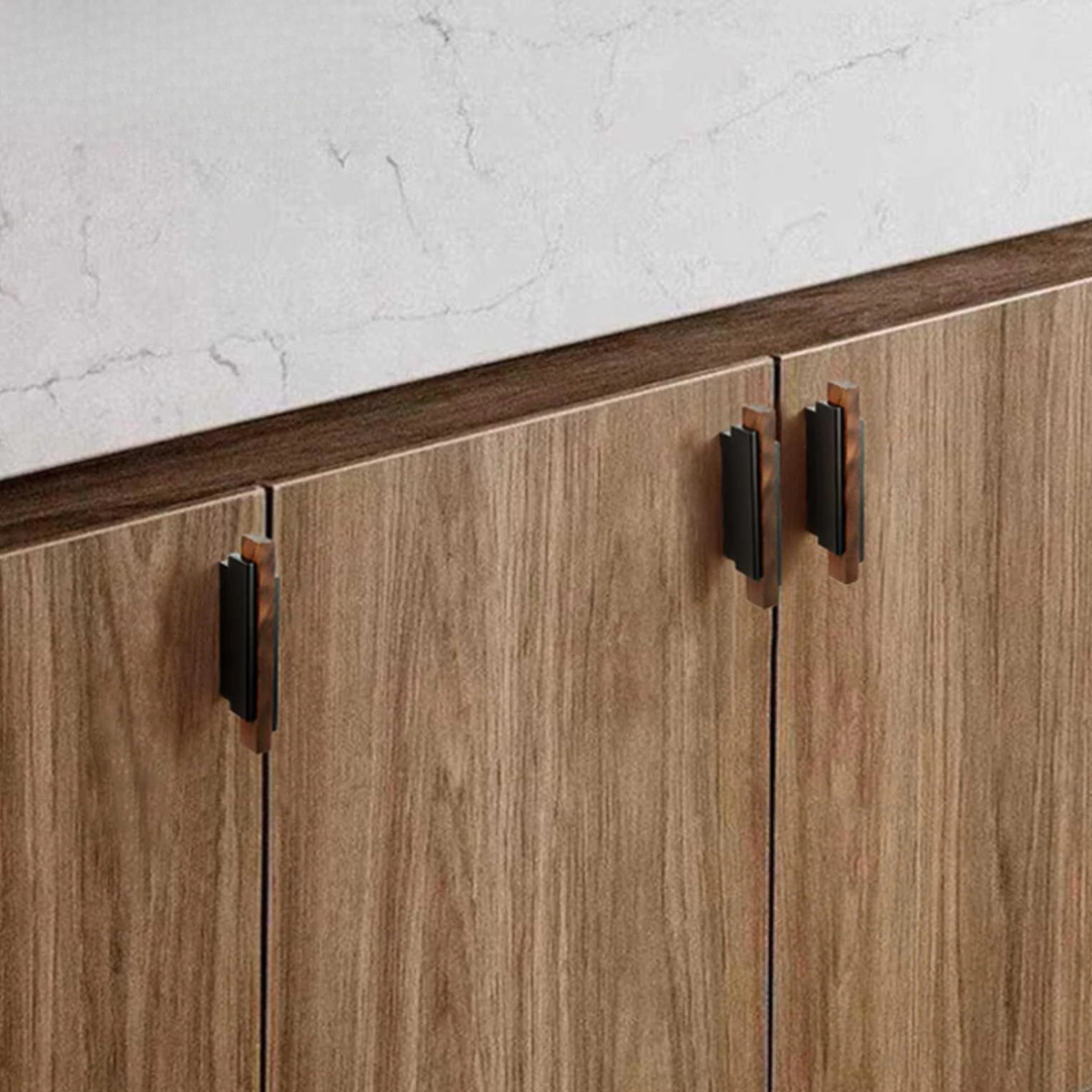 Two modern bronze handles mounted on a light oak cabinet in a minimalist interior.