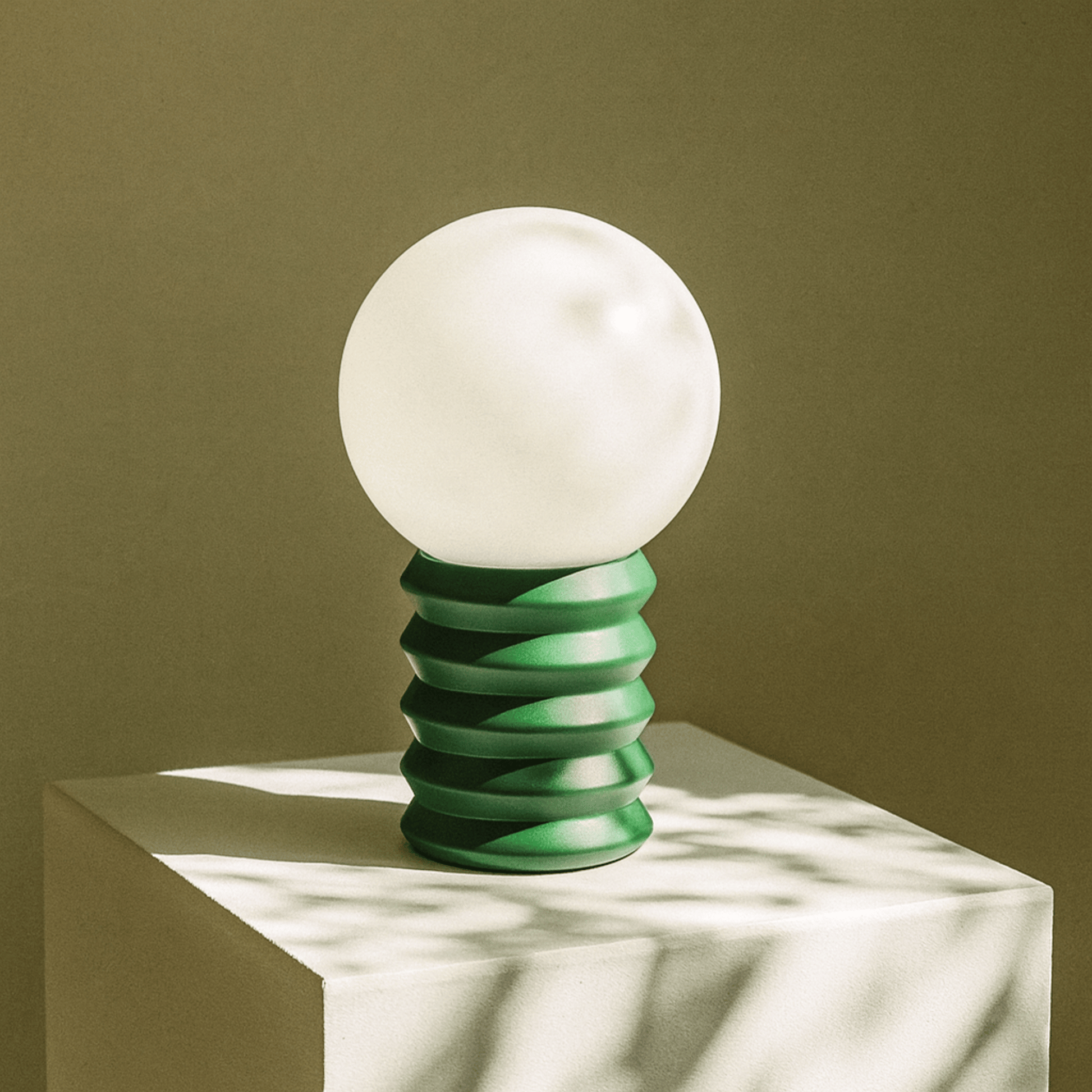 Table lamp with a white globe and green spiral base on a neutral background