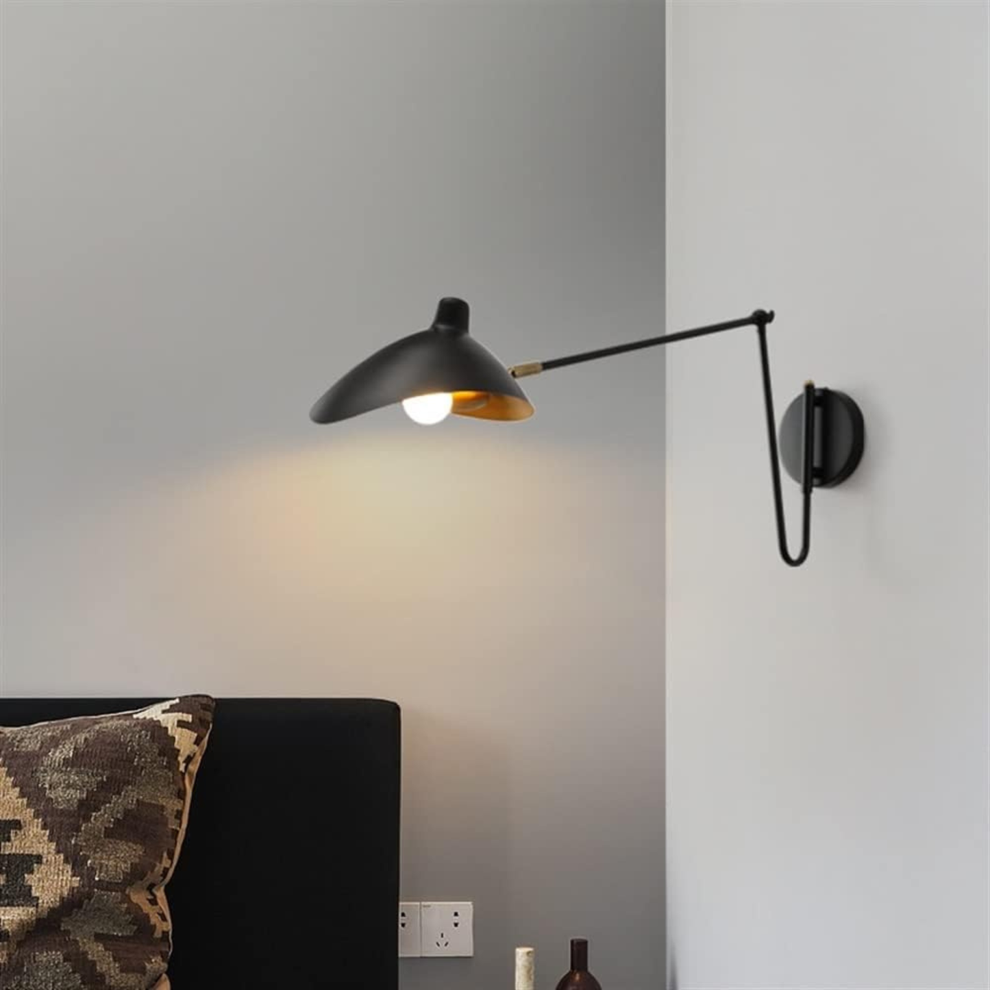 Long black swing-arm wall lamp over a bed with patterned cushions, emitting warm directional light.