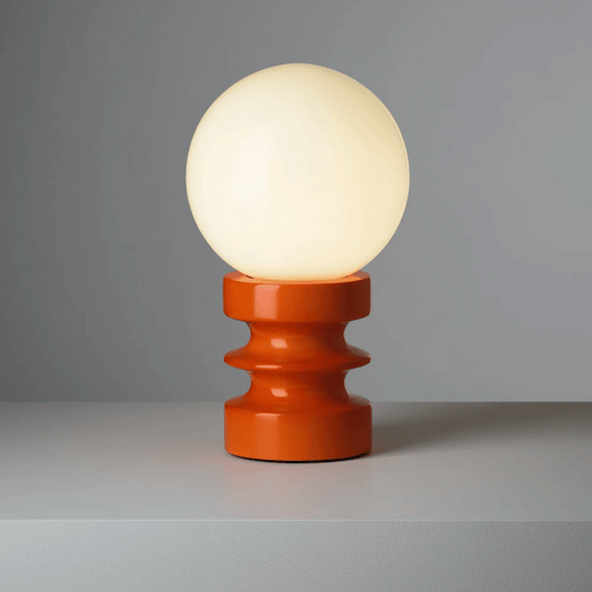 Table lamp with a round white bulb and orange base on a gray background