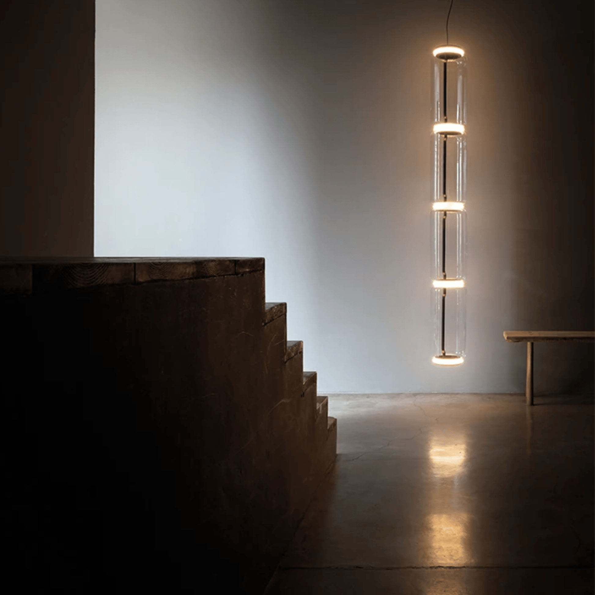 Modern staircase with a hanging cylindrical light fixture in a minimalistic setting.