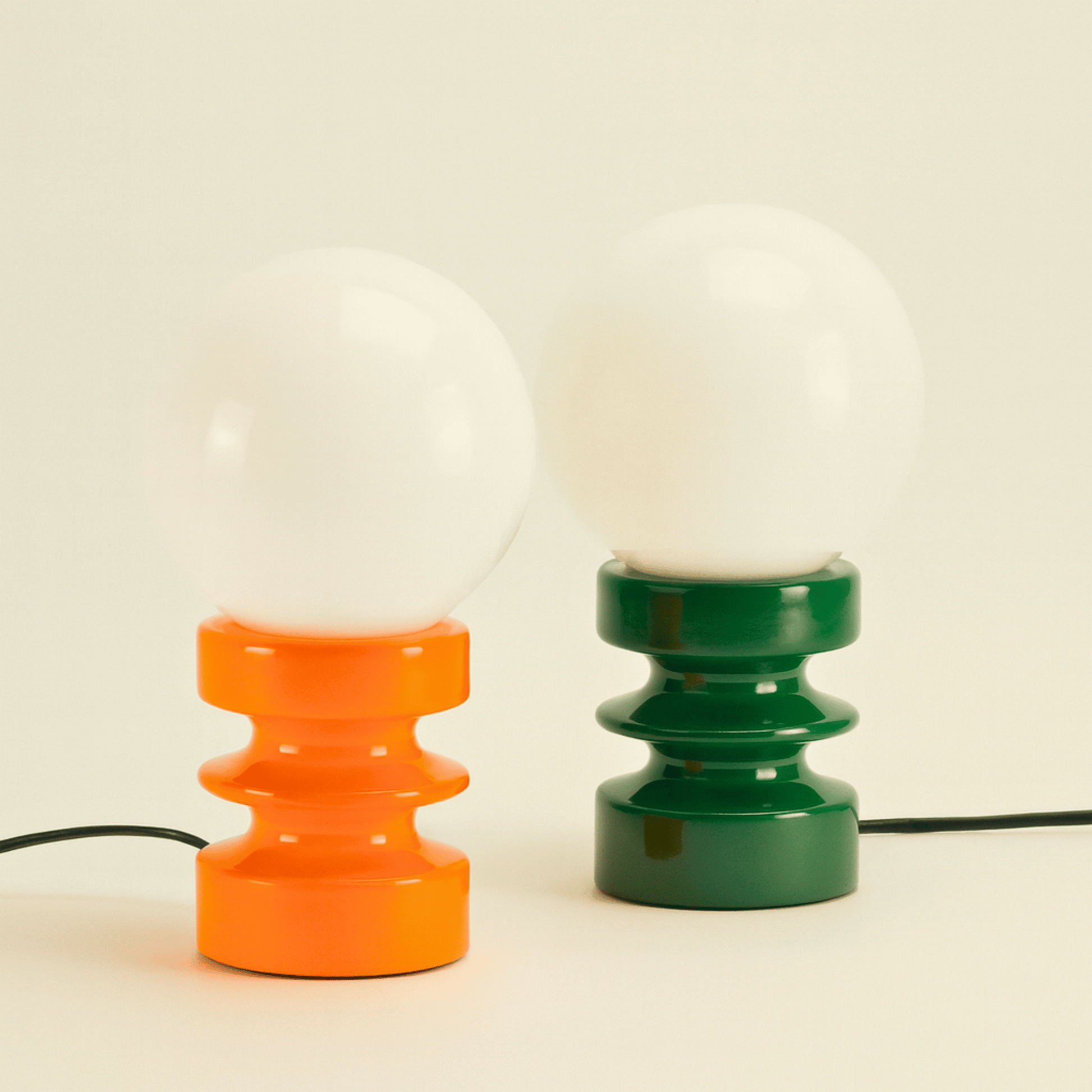 Two table lamps with orange and green bases on a beige background