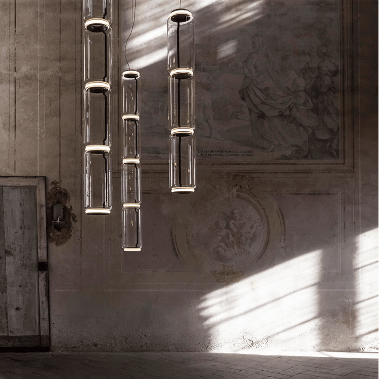 Modern chandelier hanging in a room with sunlight casting shadows on the wall.